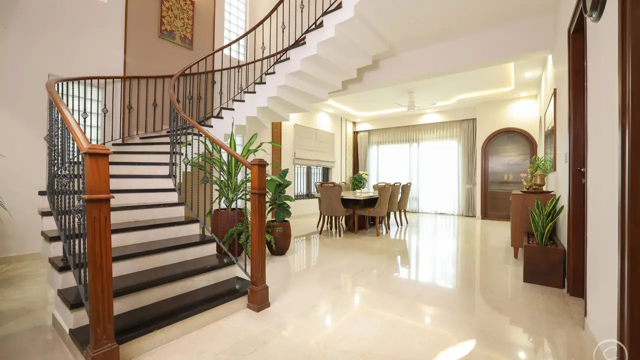 Double-height villa hall with a curved staircase and dining beyond